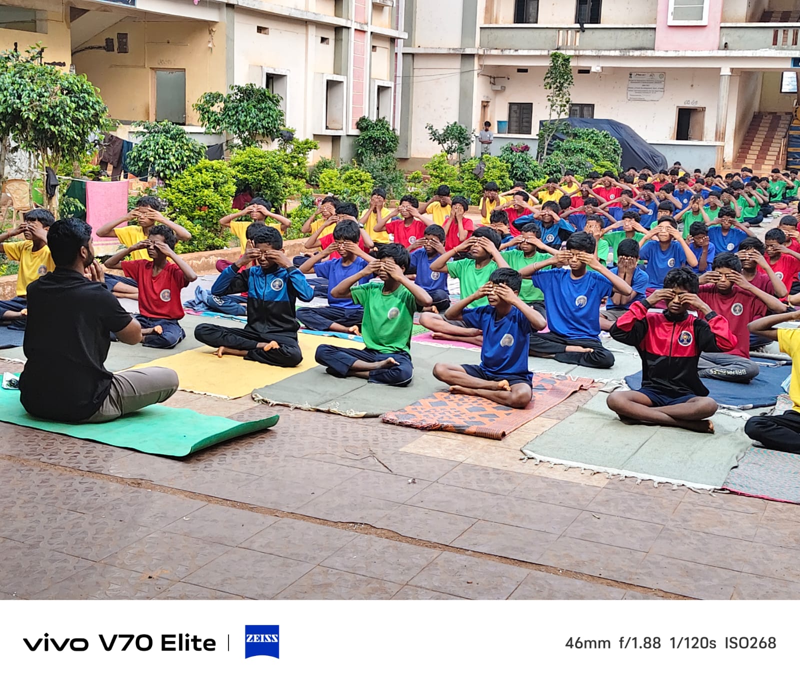 Large group of EMRS Ananthagiri students seated on mats in the campus courtyard during a morning yoga session